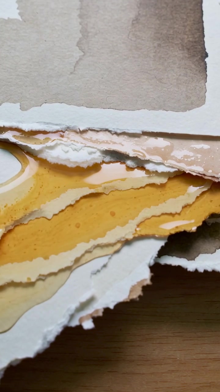 Vertical video: Camera revealing torn watercolor paper stack on desk, yellow wash flowing