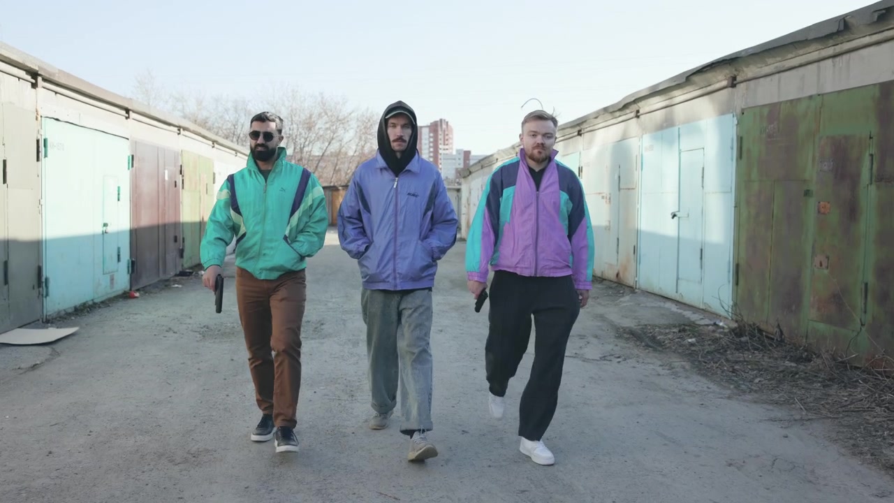 Tre uomini che camminano con passo deciso in una corsia di garage, indossando giacche a vento colorate, con una felpa con cappuccio al centro e un'andatura sicura, cinematografico.