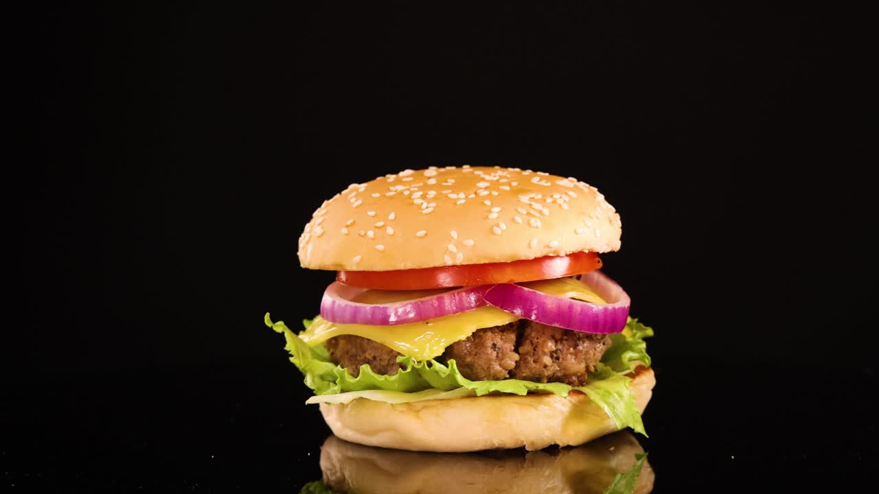 A classic beef burger with lettuce, tomato, onion, and sesame seed bun rotates smoothly under bright studio lighting against a seamless black background