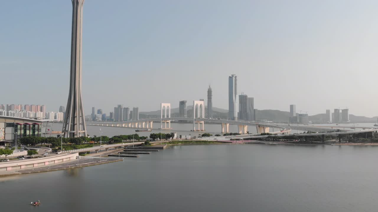 Drone shot passing Macau Tower with traffic crossing Sai Van Bridge in Macau and mainland China skyscrapers in background