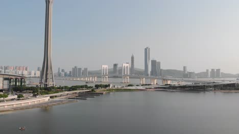 drone shot passing macau tower with traffic crossing sai van bridge in macau and mainland china skyscrapers in background