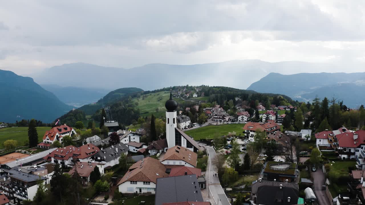 Orbiting drone shot of a Catholic church sitting amidst Italy's town of Oberbozen