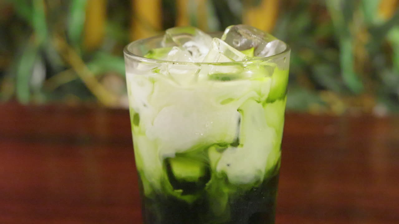 la crema se vierte lentamente en una refrescante bebida de té verde matcha, el control deslizante se cierra en cámara lenta 4k