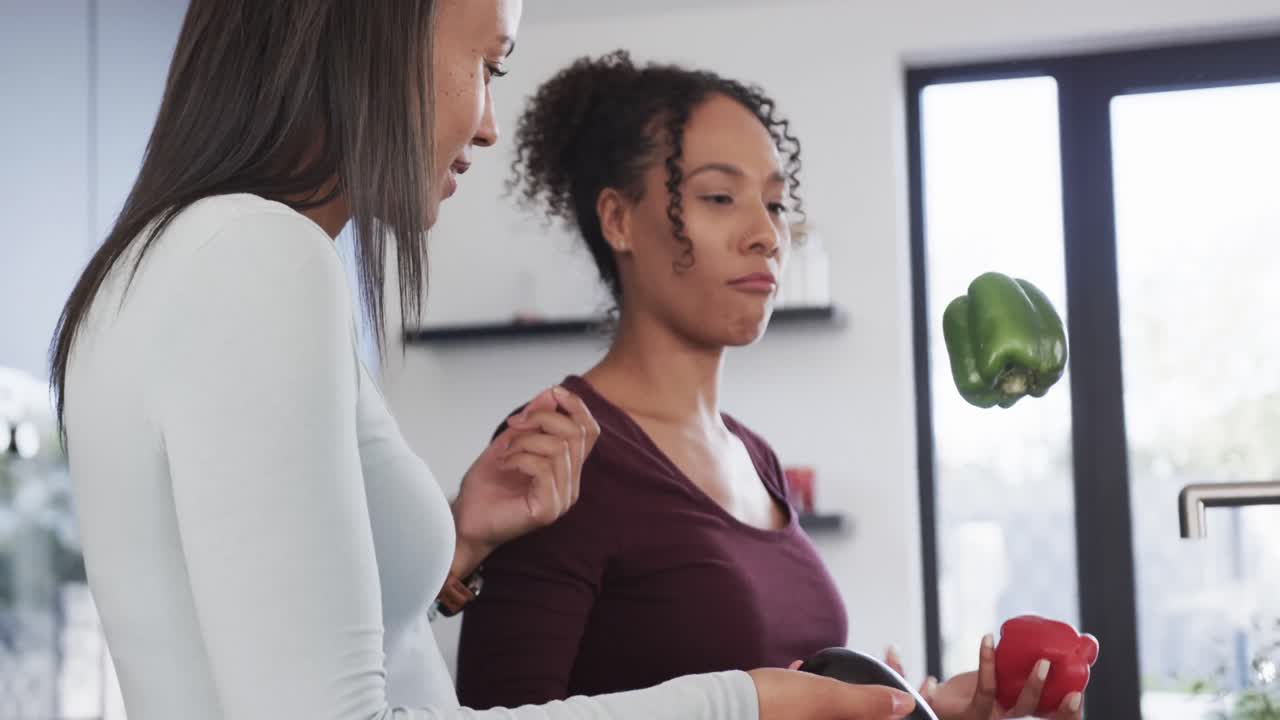 feliz pareja de lesbianas biraciales desempaquetando las compras de comestibles y hablando en la cocina, en cámara lenta