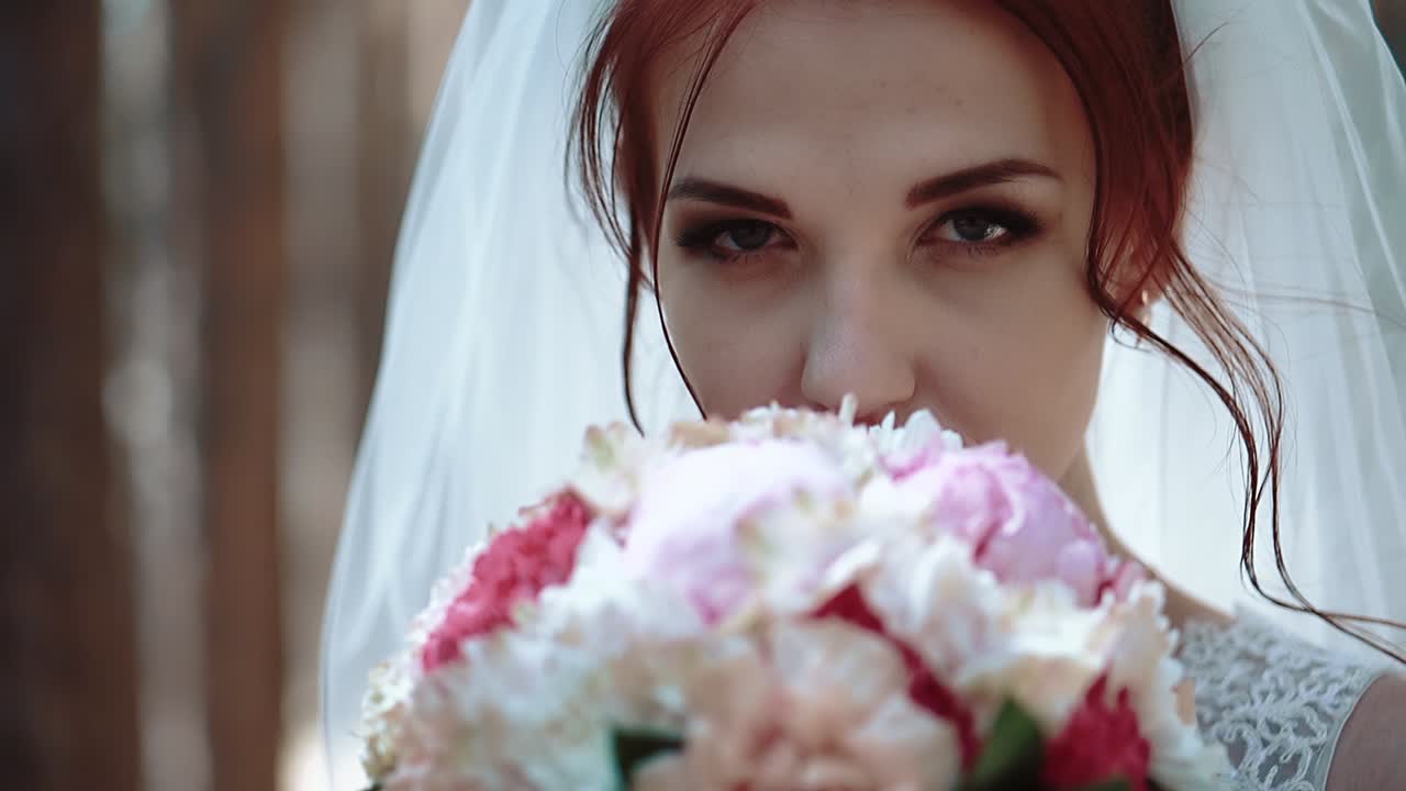 bruid kijkt naar de camera houdt een boeket bloemen bij haar gezicht dan verwijdert het portret close-up slow motion