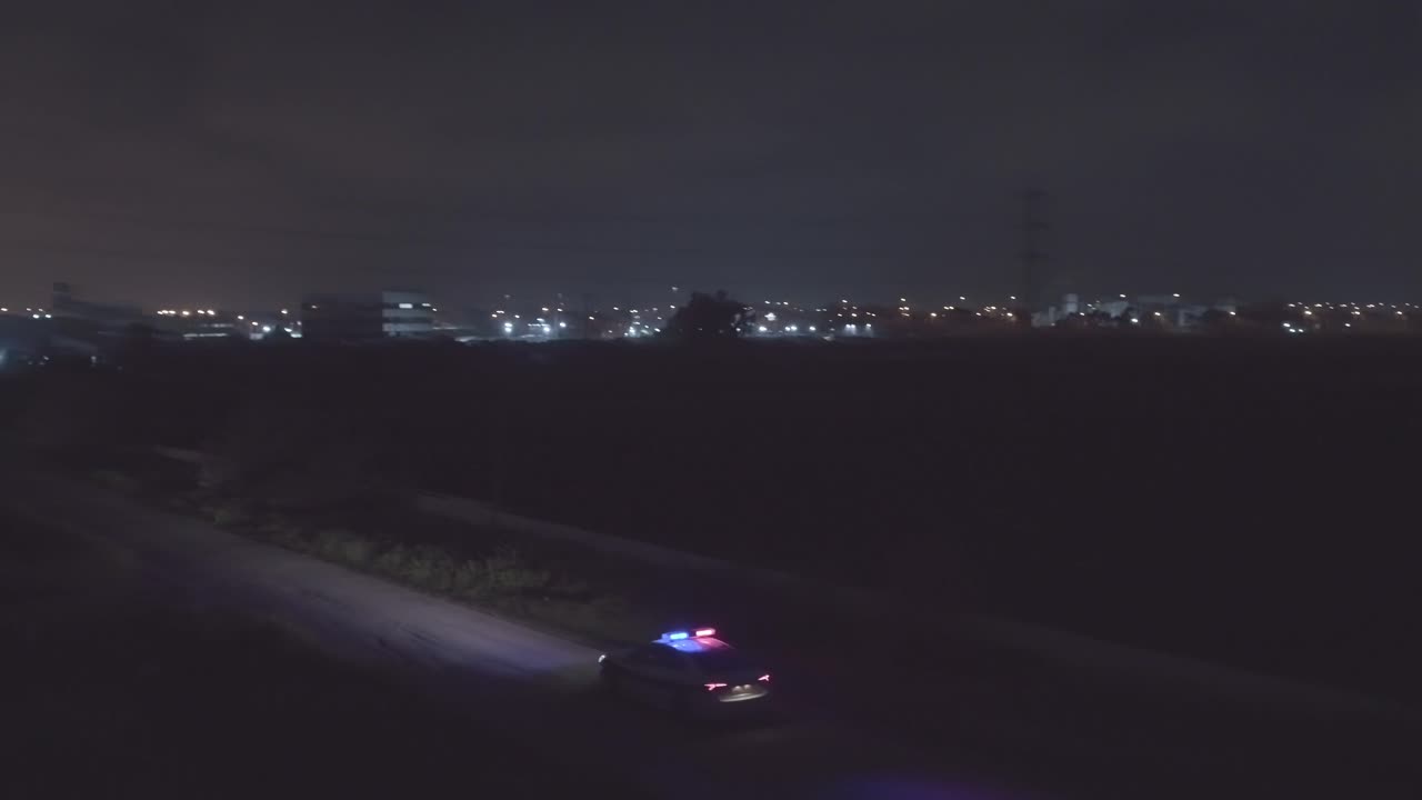 Night aerial footage of a police car driving down a dark urban area