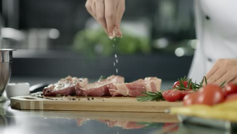 Male-chef-salting-meat-at-kitchen.-Closeup-chef-hands-salting-steak-at-workplace