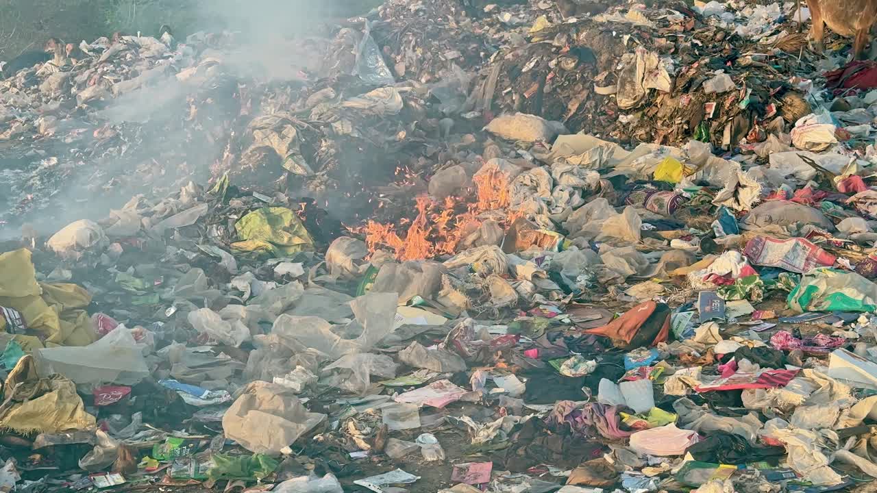 wide shot of fire burning the garbage at the dump yard or land fill outside the city and polluting the air and environment