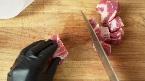 Chef-is-dicing-fresh-boneless-pork-ribs,-using-black-gloves-and-sharp-chef-knife