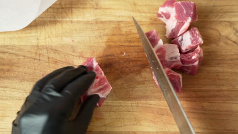 el chef está cortando costillas de cerdo frescas y deshuesadas, usando guantes negros y un cuchillo de chef afilado