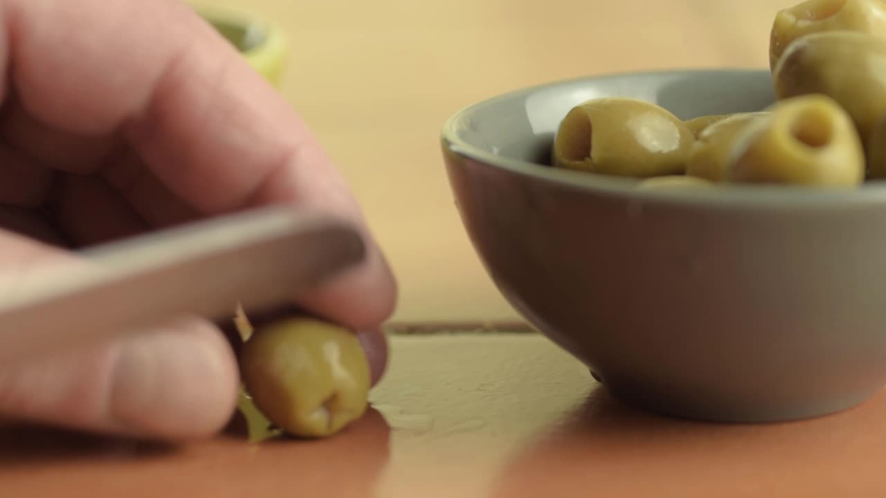 Slicing green olives with knife macro shot