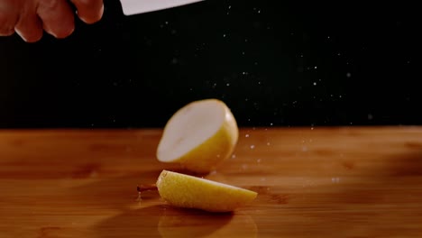 sharp knife cutting wet pear with flying water drops on wooden board, super slow motion