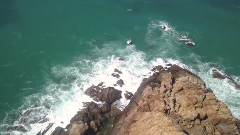 aerial tilt down shot of a cape with the waves hitting the rocks in the south of spain