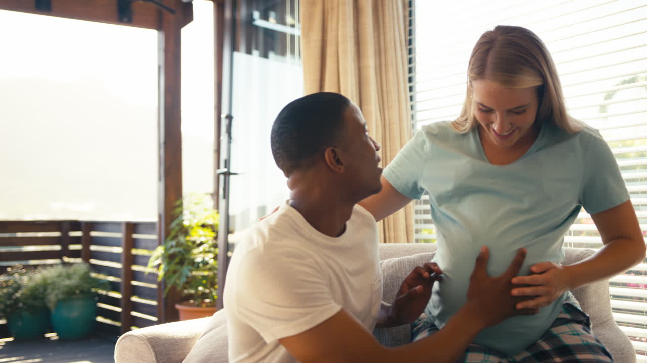 Couple With Pregnant Woman In Bedroom At Home With Man Listening To Baby's Heartbeat