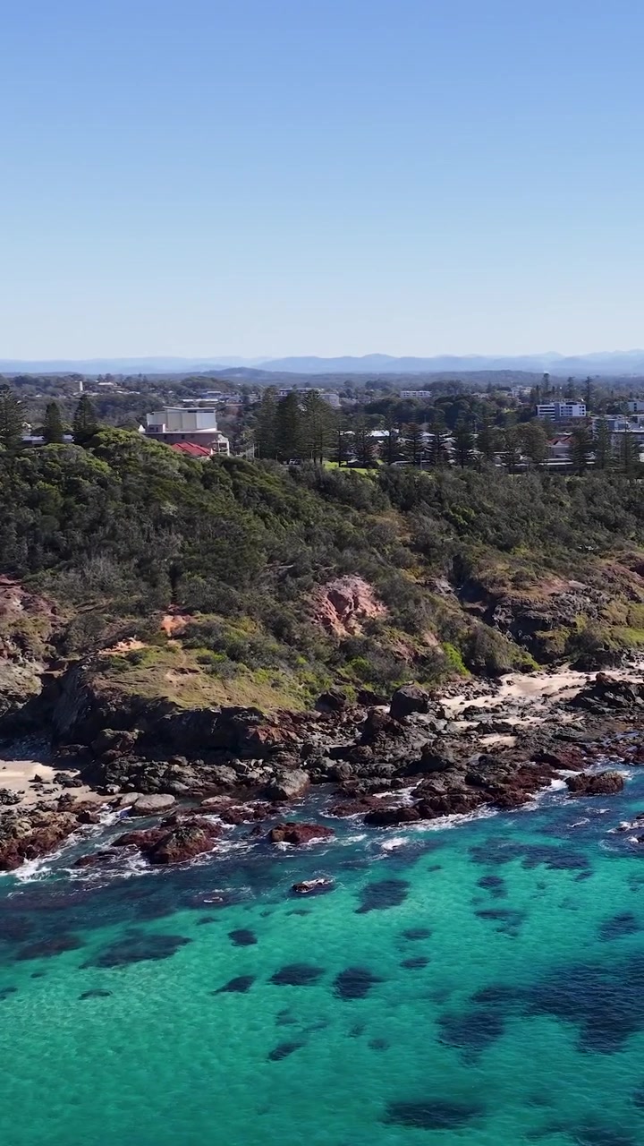Avustralya'nın Port Macquarie kentinde kayalık falezlere çarpan berrak turkuaz suyun yüksek açılı drone çekimi.