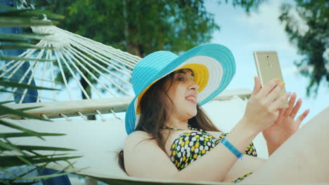 una linda morena con un sombrero de ala ancha y en bikini disfruta relajándose en el balneario leyendo
