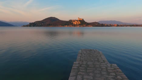 peaceful scene of concrete pier on lake maggiore calm water in italy, angera castle on background