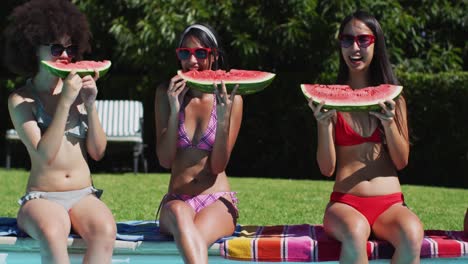 retrato de un grupo de niñas diversas comiendo sandía sentadas junto a la piscina