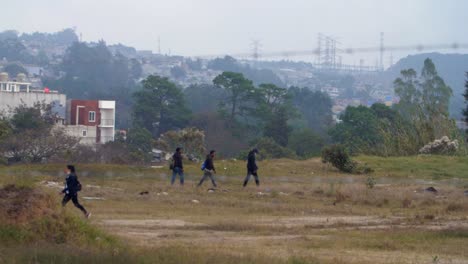 Street view with eerie atmosphere through barbed wire fence, people crossing field, favelas Zone 18 Guatemala City, Guatemala