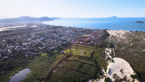 escena aérea drone playa paradisíaca florianópolis vista desde lo alto pueblo costero cerca del mar con montañas dunas horizonte edificios fraccionamiento urbano en la costa praia dos ingles