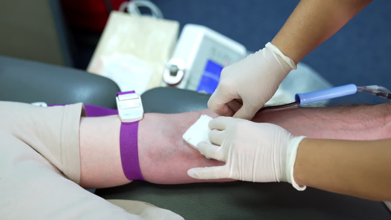 Tourniquet is attached to the forearm of a donor. Gloved hands of a nurse insert a catheter needle into the vein of a person. Close up.