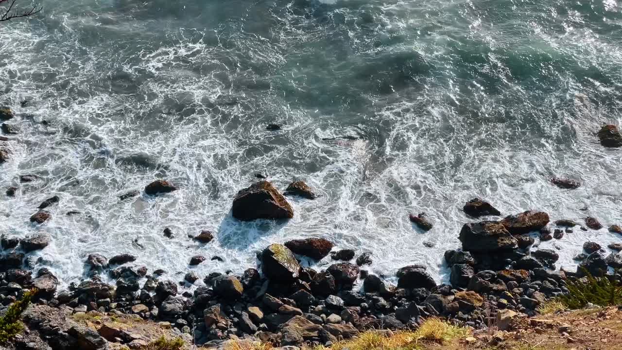 Vista dall'alto di onde che si infrangono su una costa rocciosa. Inquadratura dall'alto dell'acqua dell'Oceano Pacifico che colpisce rocce e pietre scure sulla riva.