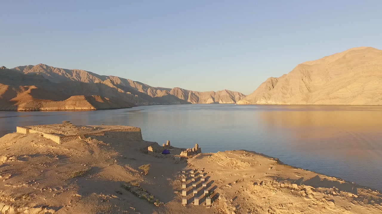 Drone shot rising from the ruins on Telegraph Island in the Strait of Hormuz between Oman and Iran, a strategic maritime chokepoint and major global oil shipping route connecting the Persian Gulf