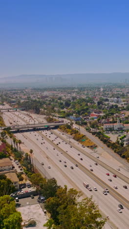 quickly moving cars by the multi-lane freeways of los angeles, california, usa. amazing clear blue sky at backdrop. rising drone footage. vertical video