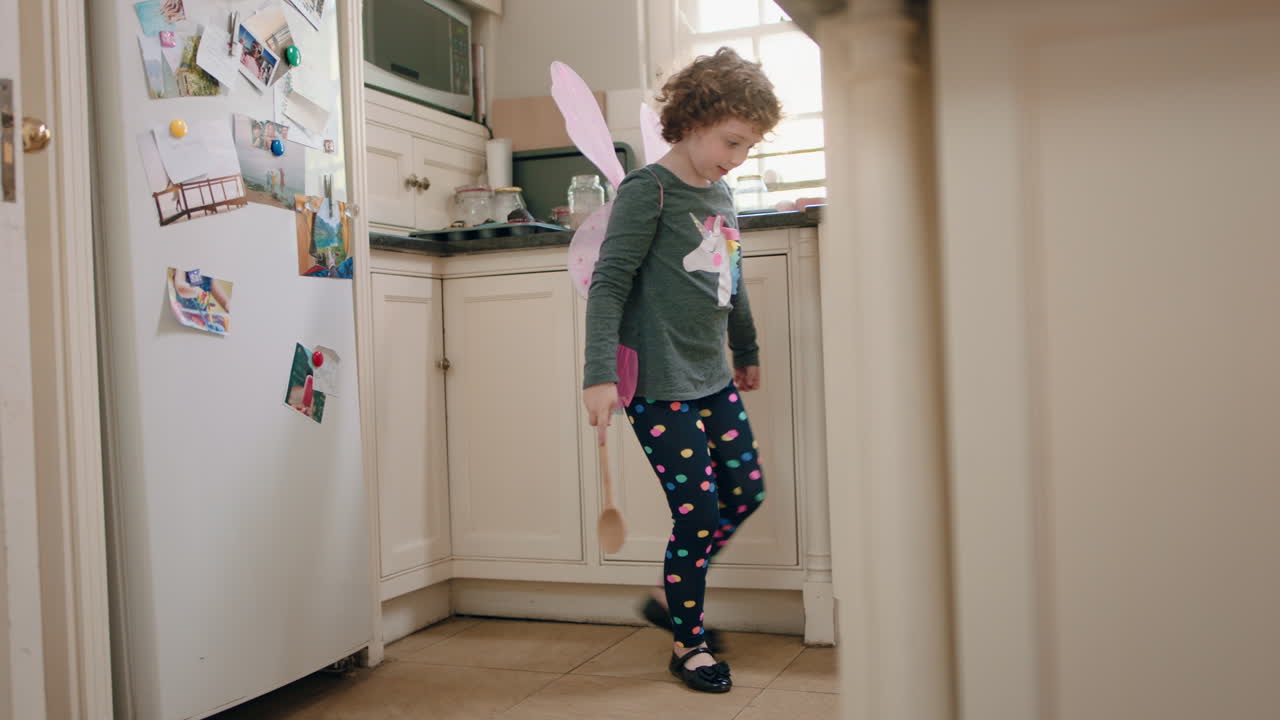 happy little girl dancing in kitchen wearing cute fairy wings having fun waving spoon playing pretend doing funny dance moves enjoying weekend at home