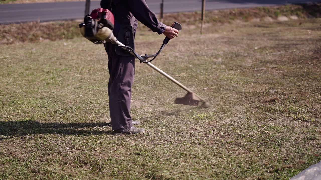 Person operating a string trimmer to cut grass