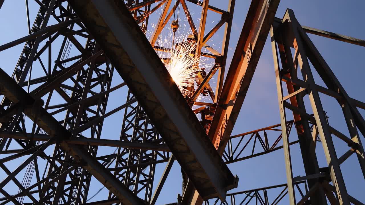 Wide-angle video of a construction site with towering steel frameworks and workers in safety gear