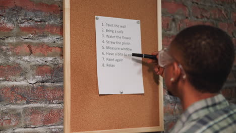 hombre negro con gafas lee la lista de tareas pendientes en el tablero de corcho