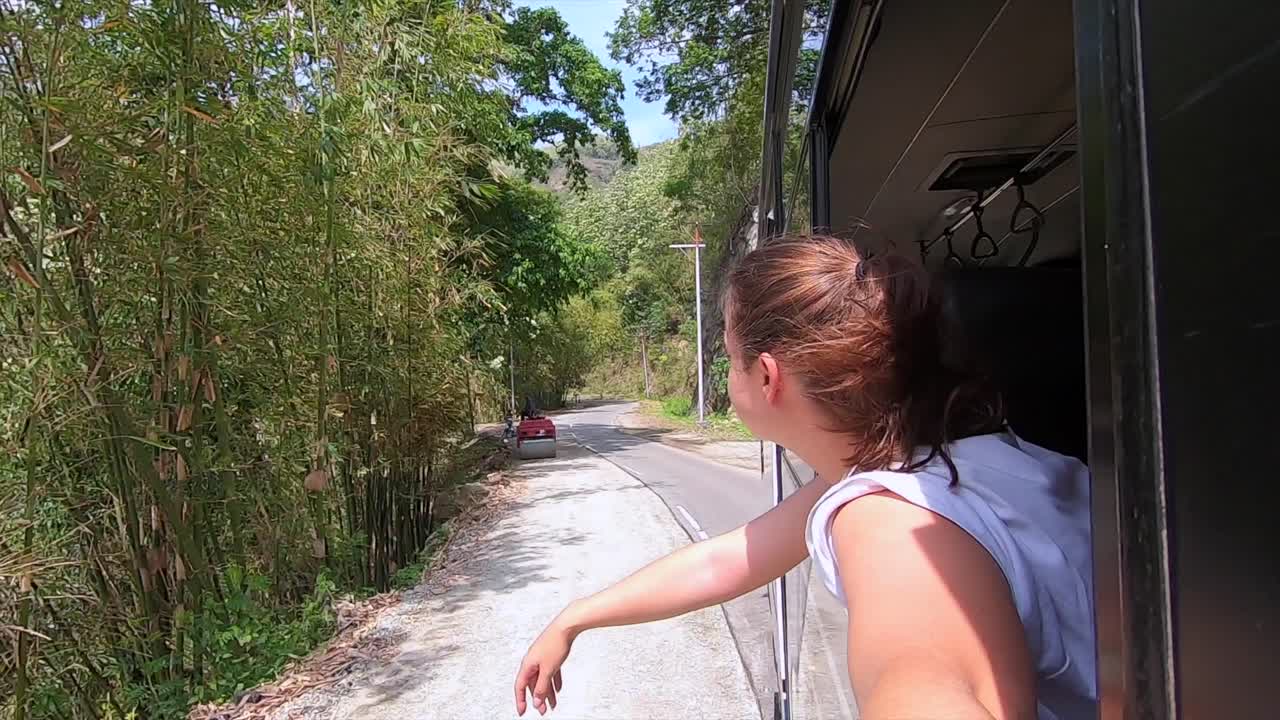 Beautiful woman leaning out of the bus window and enjoying the fresh breeze and freedom on her travel journey in Indonesia.