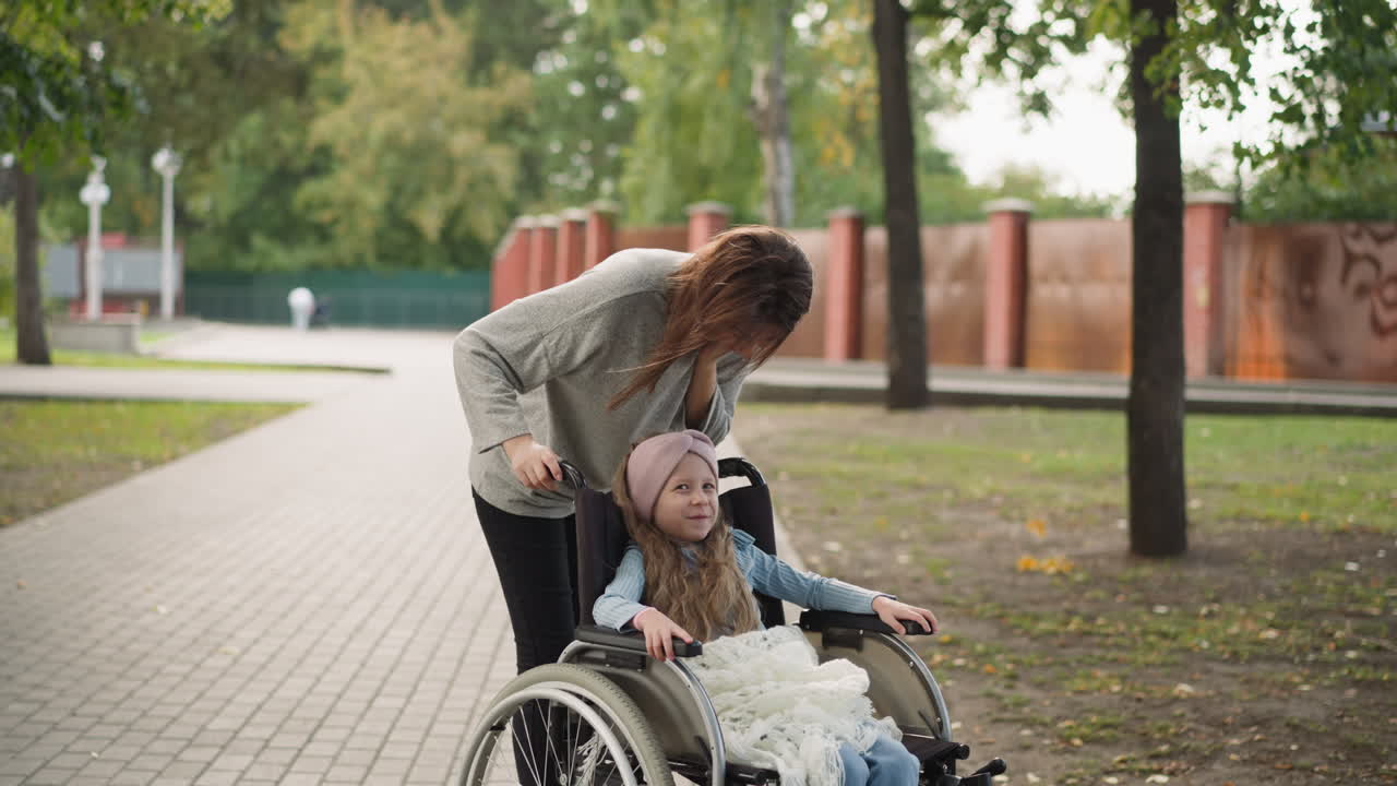 madre feliz besa a su hija sentada en silla de ruedas en la calle