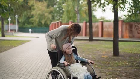 madre feliz besa a su hija sentada en silla de ruedas en la calle