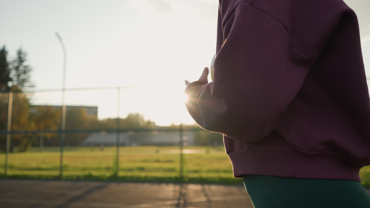뒷면과 초록색에서 아름다운 빛을 만드는 빛과 함께 야외에서 배구 공을 뛰는 여성의 근접 측면 뷰, 활동적인 생활 방식과 야외 스포츠를 보여줍니다.