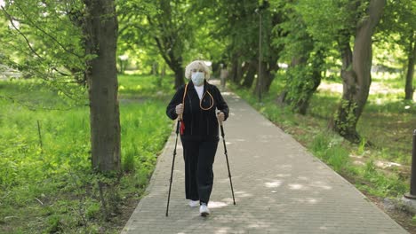 active senior old woman in mask training nordic walking in park at quarantine