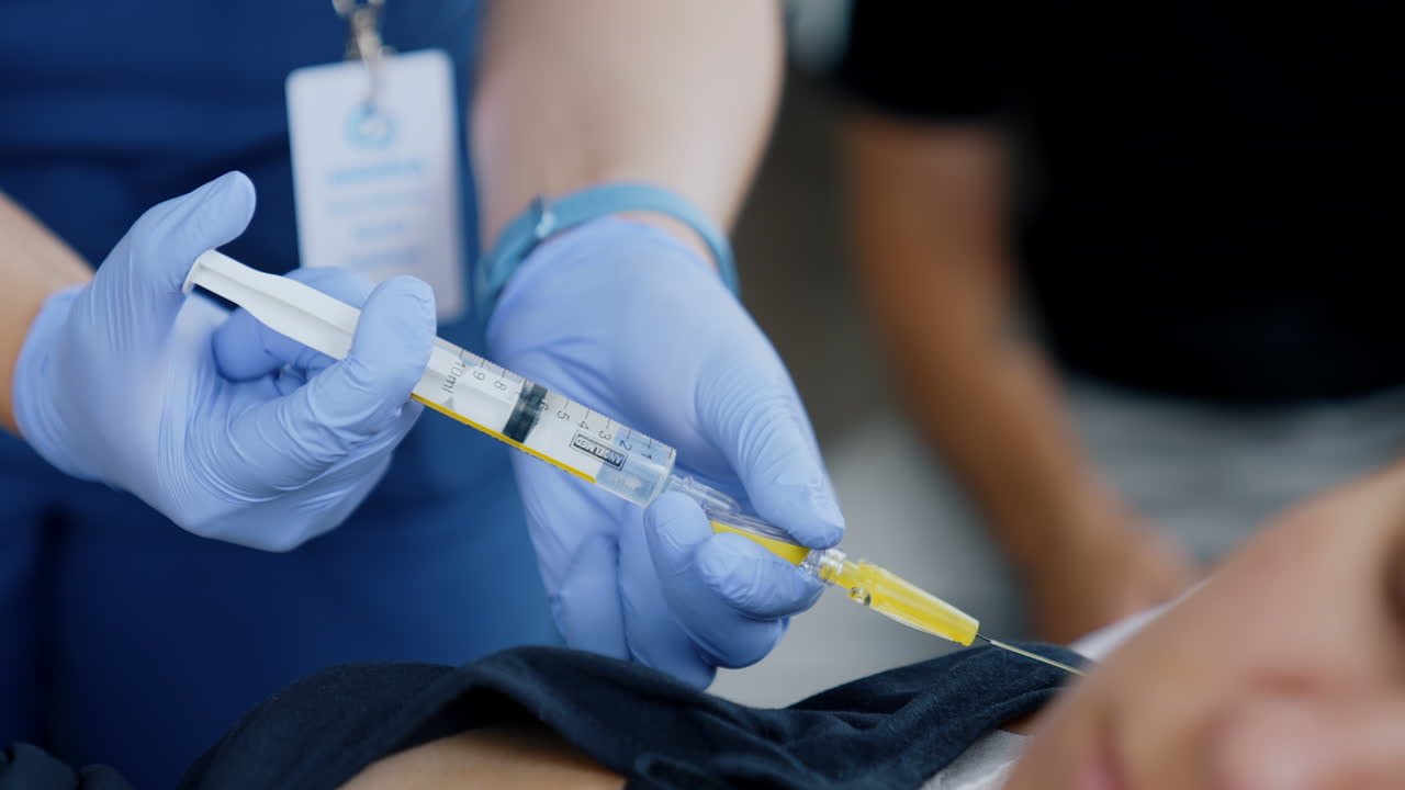 Hands in latex blue gloves holding a syringe. Giving injection to a patient. Close up.