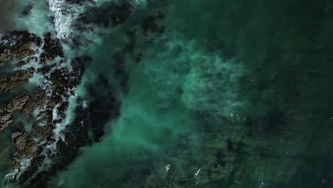 aerial shot of waves rolling in and crashing against the rocks and shore in iquique