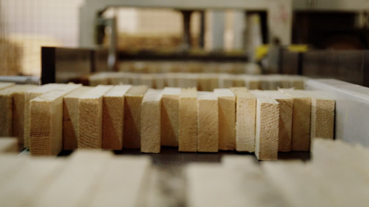 A close-up of an automated machine assembling small wooden blocks. A pusher arm arranges the components on a production line, creating an engineered wood panel for construction
