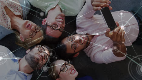 animation of dots connecting with lines over man taking selfie with coworkers while lying on floor