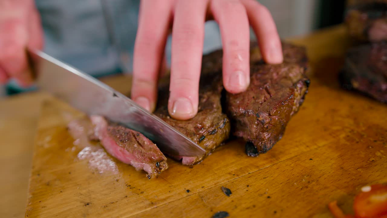 커팅 보드에 육즙이 풍부한 구운 쇠고기 스테이크를 자르는 칼로 남성 손의 보기를 닫습니다