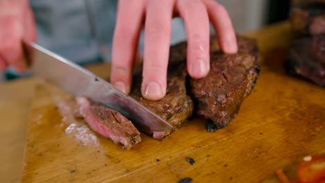 close up view of male hand with a knife slicing the juicy grilled beef steak on cutting board