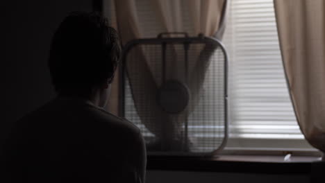 the silhouette of a young high school aged teen boy sitting on his bed