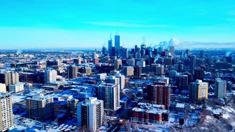 light-traffic-over-116-st-nw-and-100-Ave-NW-aerial-flyby-West-North-to-South-with-skyscrapers-in-the-horizon-assorted-residential-commercial-building-with-clear-blue-winter-sky-snow-covered-top-view