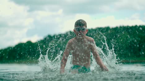 joyful kid with swim gear outburst water on the lake with hands and happily enjoying