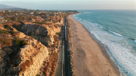 Descending-aerial-view-of-an-approaching-Amtrak-train-near-San-Clemente-State-Beach,-California