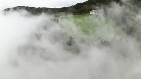 aerial view revealing a road in middle of foggy meadows and forest in tyrol, italy