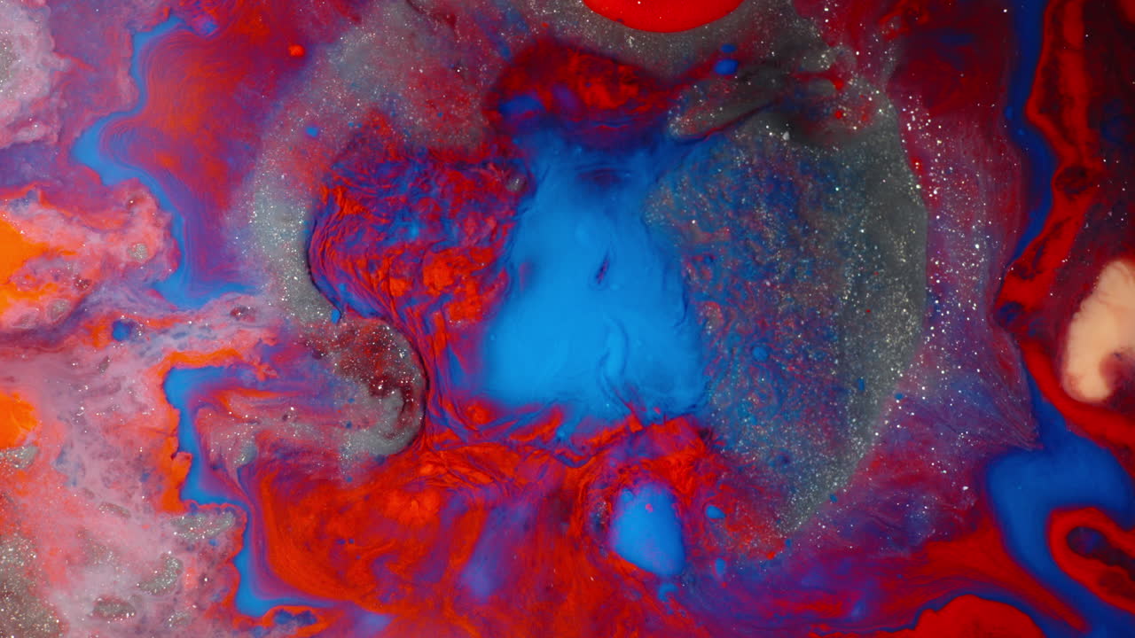 Swirling colors of red, blue, and orange ink mixing in water with sparkles creating an abstract scene