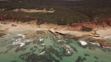 drone aerial with a long zoom in with clear blue beautiful water and rocky mars like landscape and forest